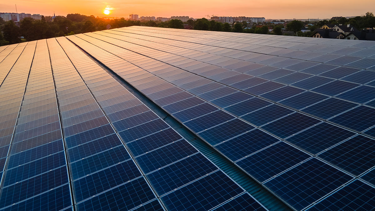 Blue Photovoltaic Solar Panels Mounted On Building Roof For Producing Clean Ecological Electricity At Sunset. Production Of Renewable Energy Concept